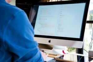 A man is sitting at a Mac computer and doing some programming tasks.