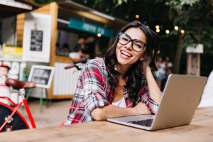 Character traits - A girl with glasses is sitting at a computer and smiling at the camera.
